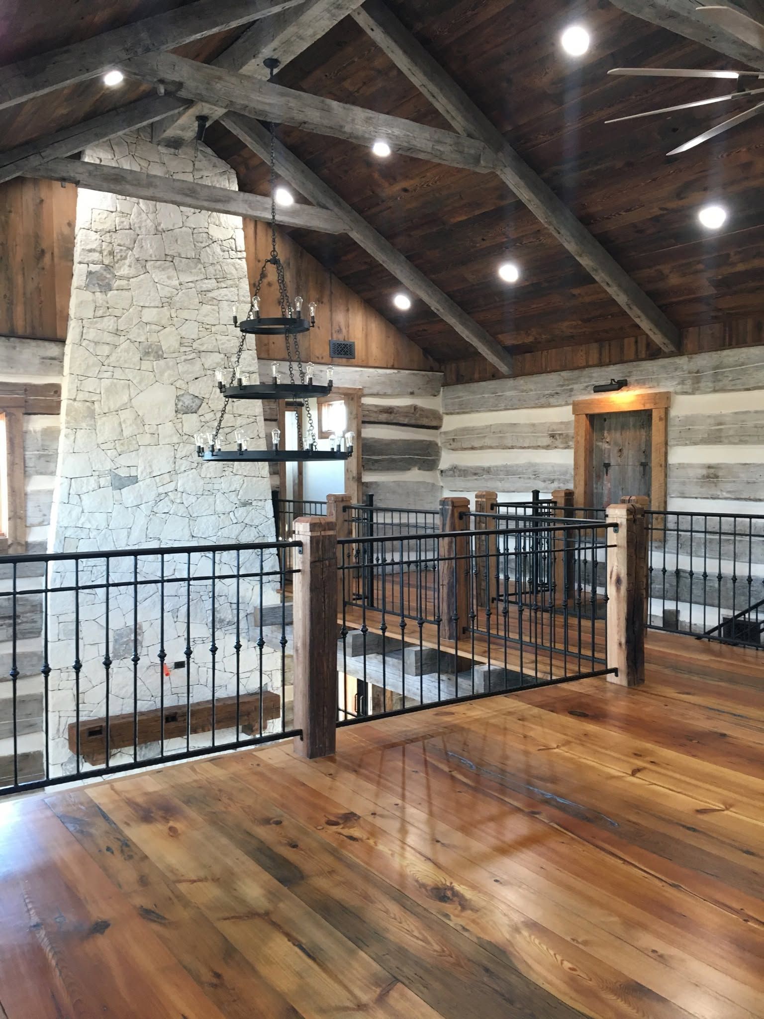 Rustic loft interior with exposed beams, stone walls, black railings, and wood floors.