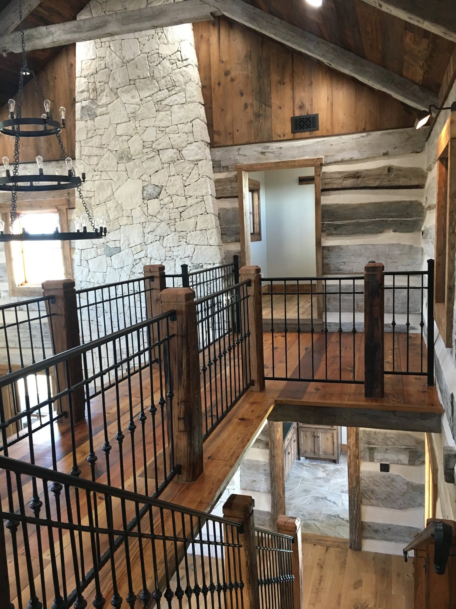 Rustic loft with black railings, exposed log walls, and a wooden staircase overlooking a lower level