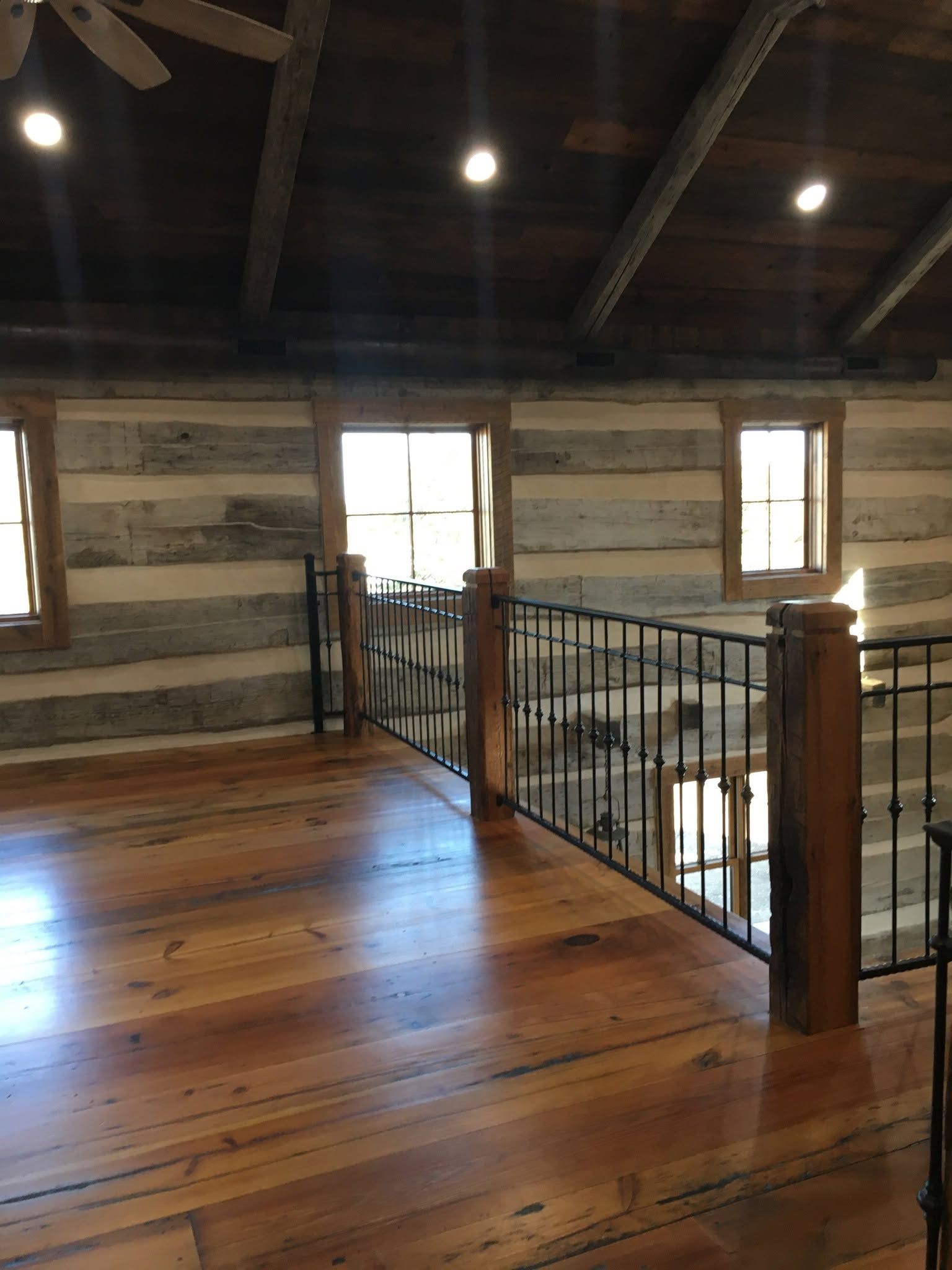 Wooden loft interior with exposed beams, railing, windows, and polished floorboards.