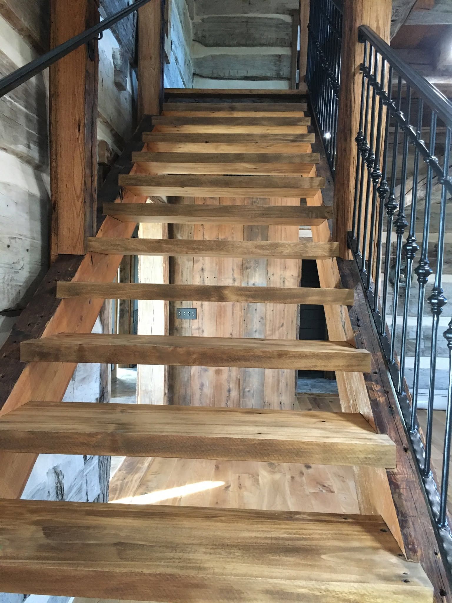 Wooden staircase under construction with exposed steps and black metal railings on both sides