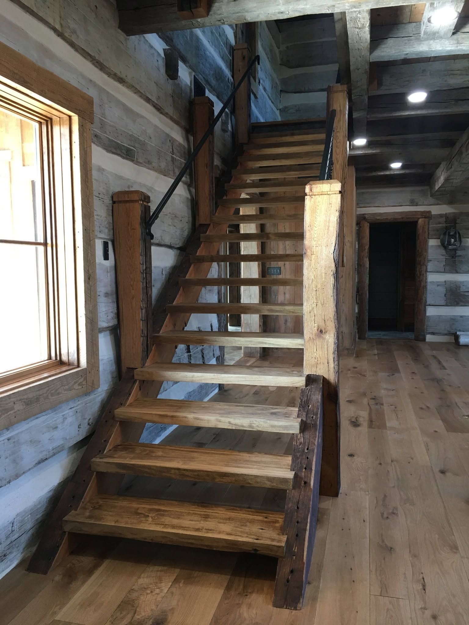 Rustic wooden staircase inside a log cabin with timber walls and a window on the left.