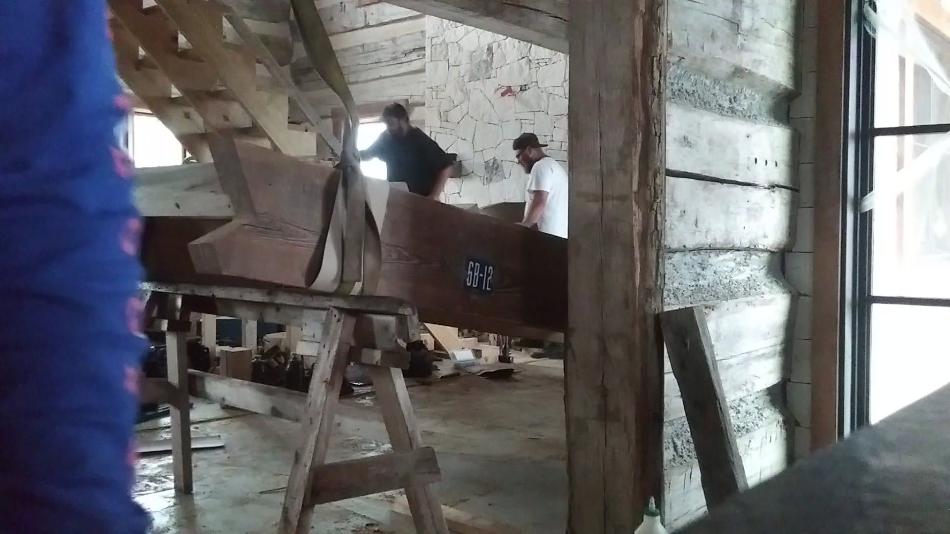 Workers loading a large brown crate inside a rustic warehouse with wooden beams and a ladder