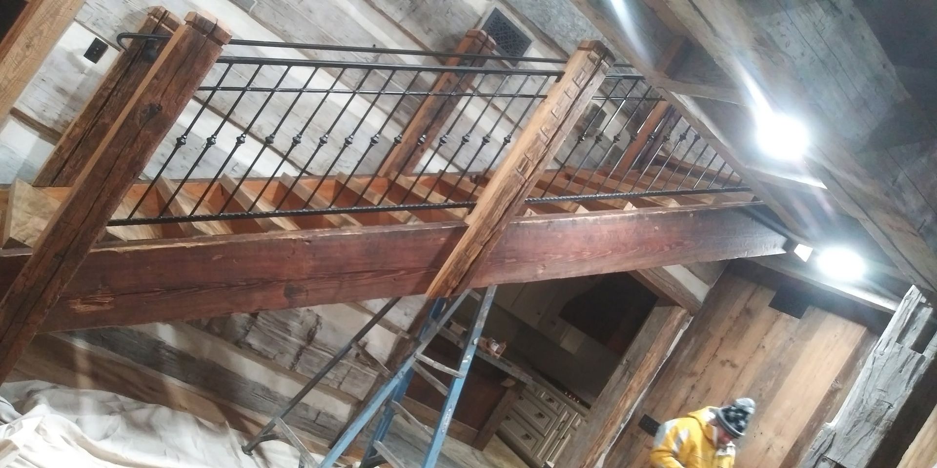 Wooden stairway inside a dusty construction site with metal railings and a worker below
