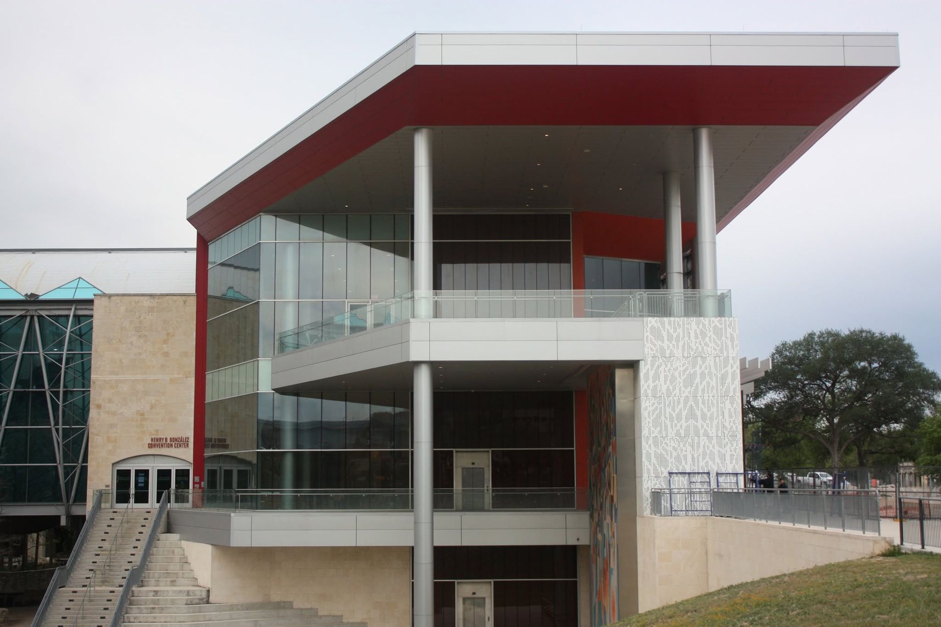 Modern building with glass walls, red roof overhang, and outdoor stairway on a campus-like setting
