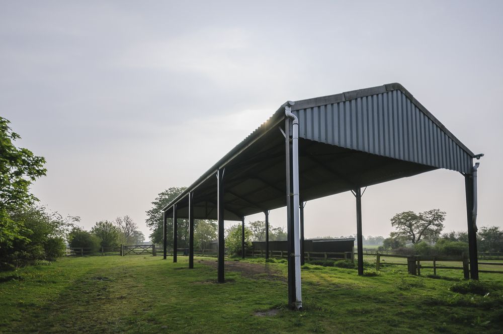 Covered metal pavilion in a grassy field under a cloudy sky