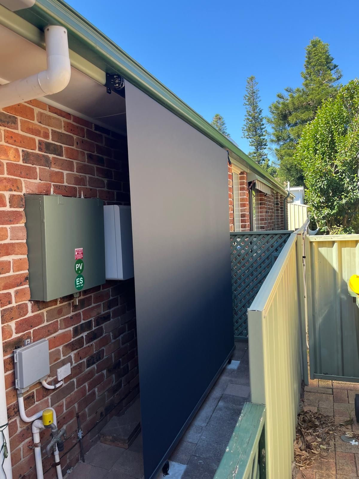 Brick house side yard with a dark utility enclosure beside a fence and air-conditioning unit.