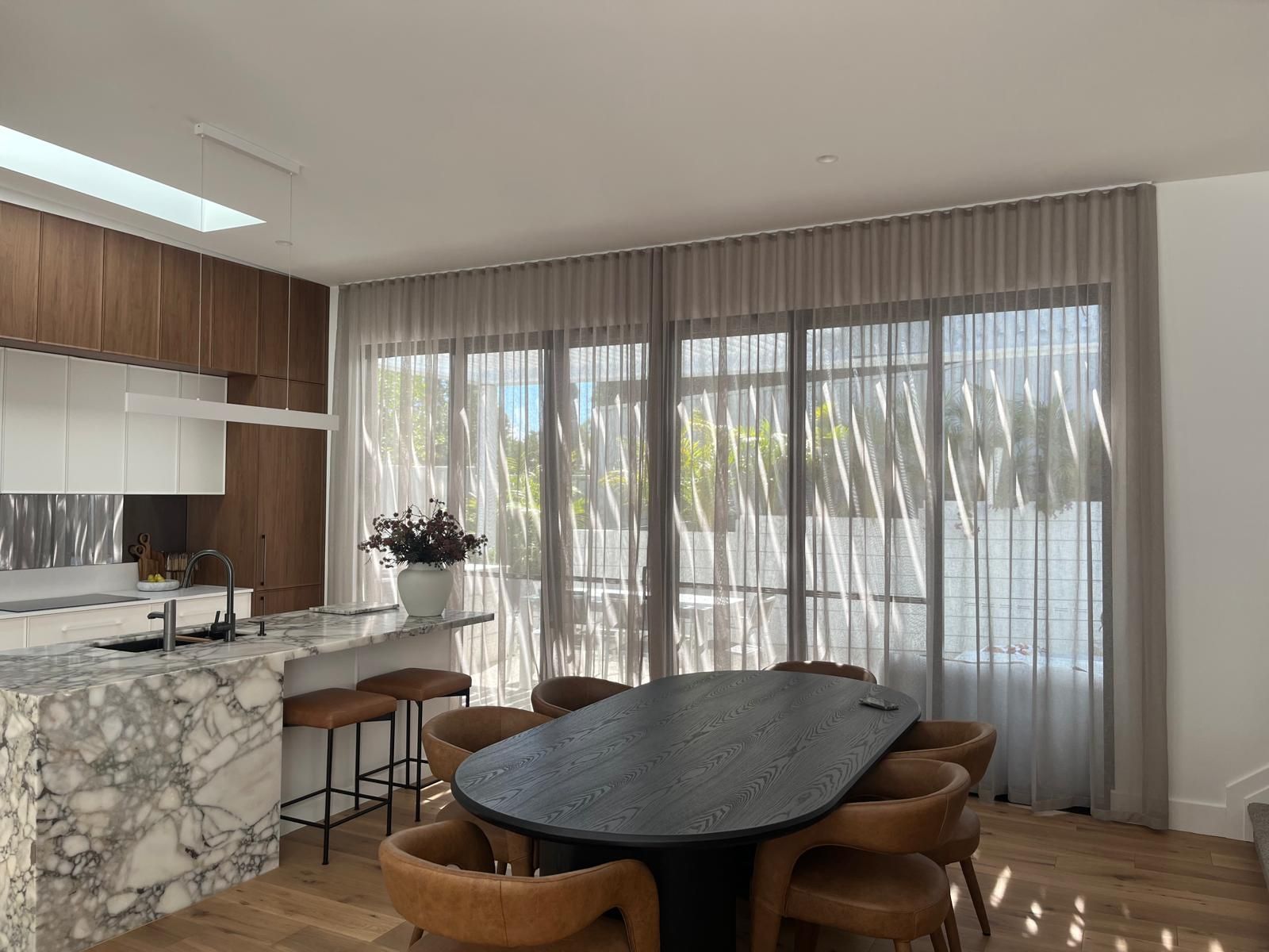 Modern kitchen and dining area with marble island, round table, and sheer curtains over sliding glass doors