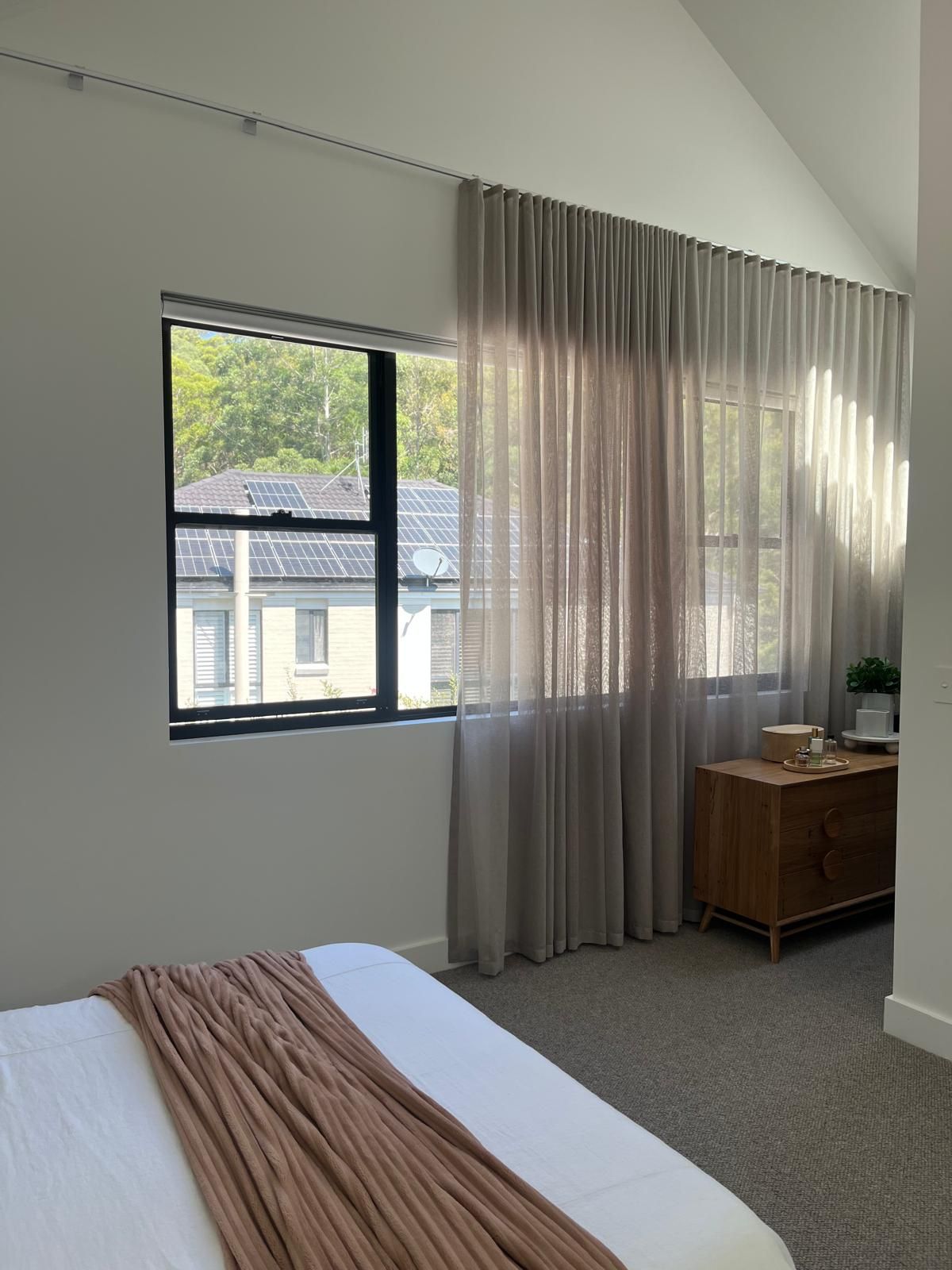 Bright bedroom with bed, large window, sheer curtains, and wooden dresser in soft natural light