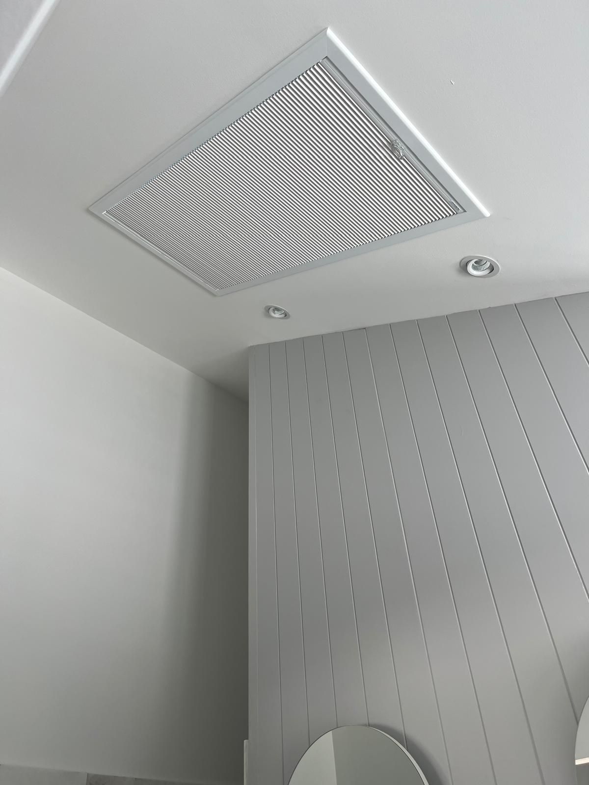 White room ceiling with a large square vent and two recessed lights above a paneled wall.