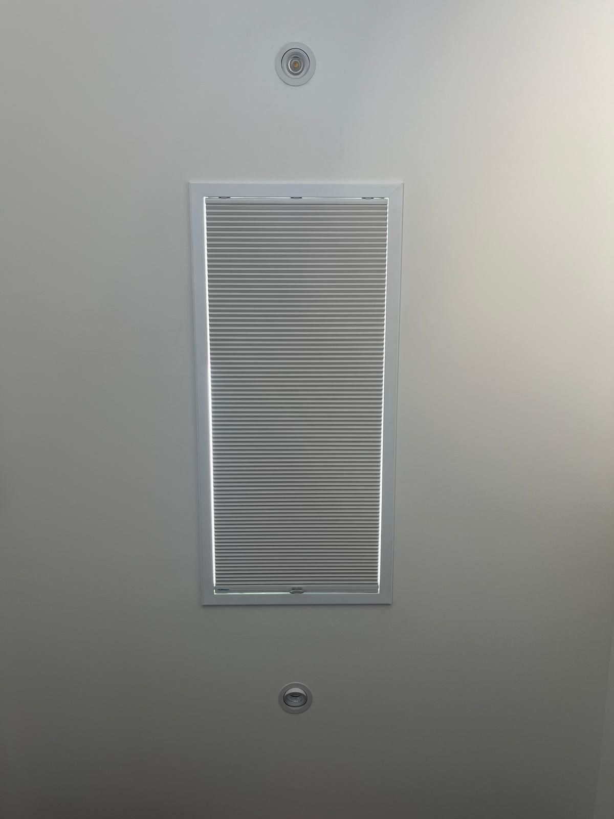 White wall vent grille centered between two screws on a light gray wall.