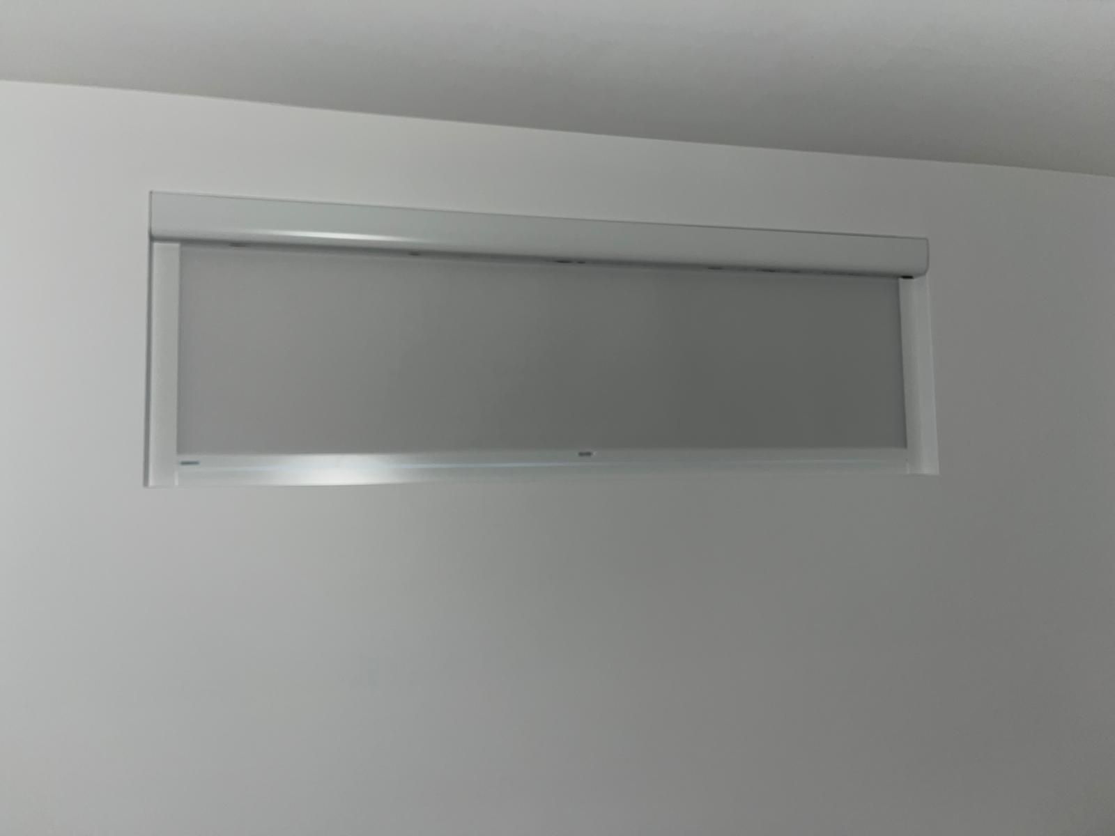 A small frosted window with a silver frame set high on a plain white wall.