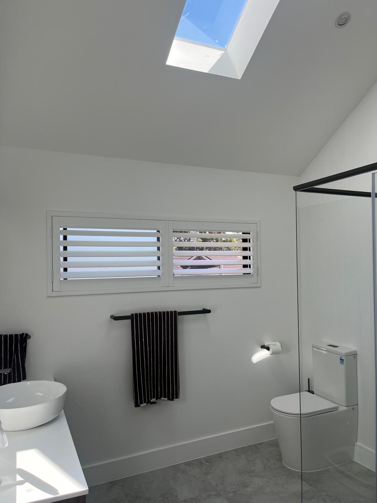 Modern bathroom with skylight, window blinds, sink, toilet, and glass shower frame