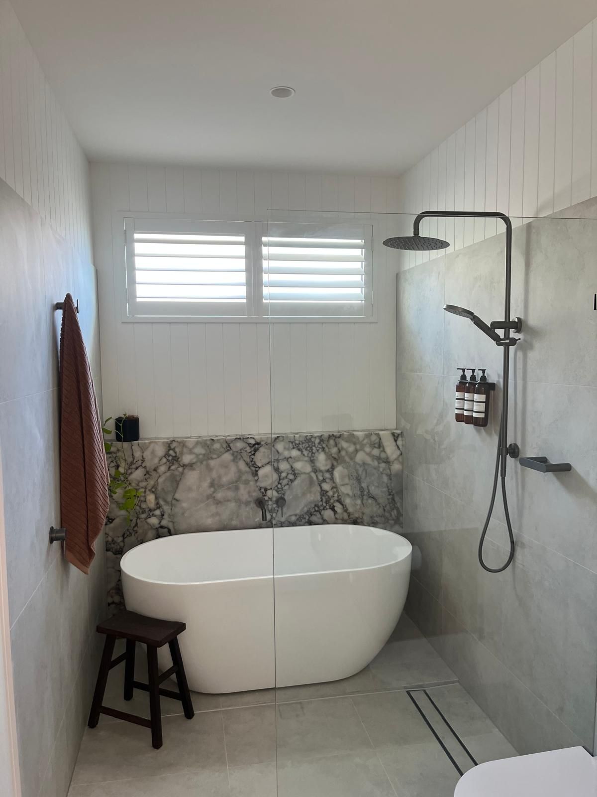 Modern white bathroom with freestanding tub, walk-in shower, and small stool under a window
