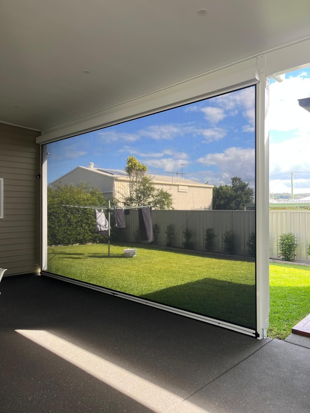 Covered patio overlooking a sunny backyard with green lawn, fence, and neighboring house