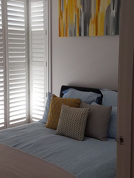 Bedroom With Bed, White Shutters, Artwork, And Colorful Pillows — Winning Blinds in Cardiff, NSW