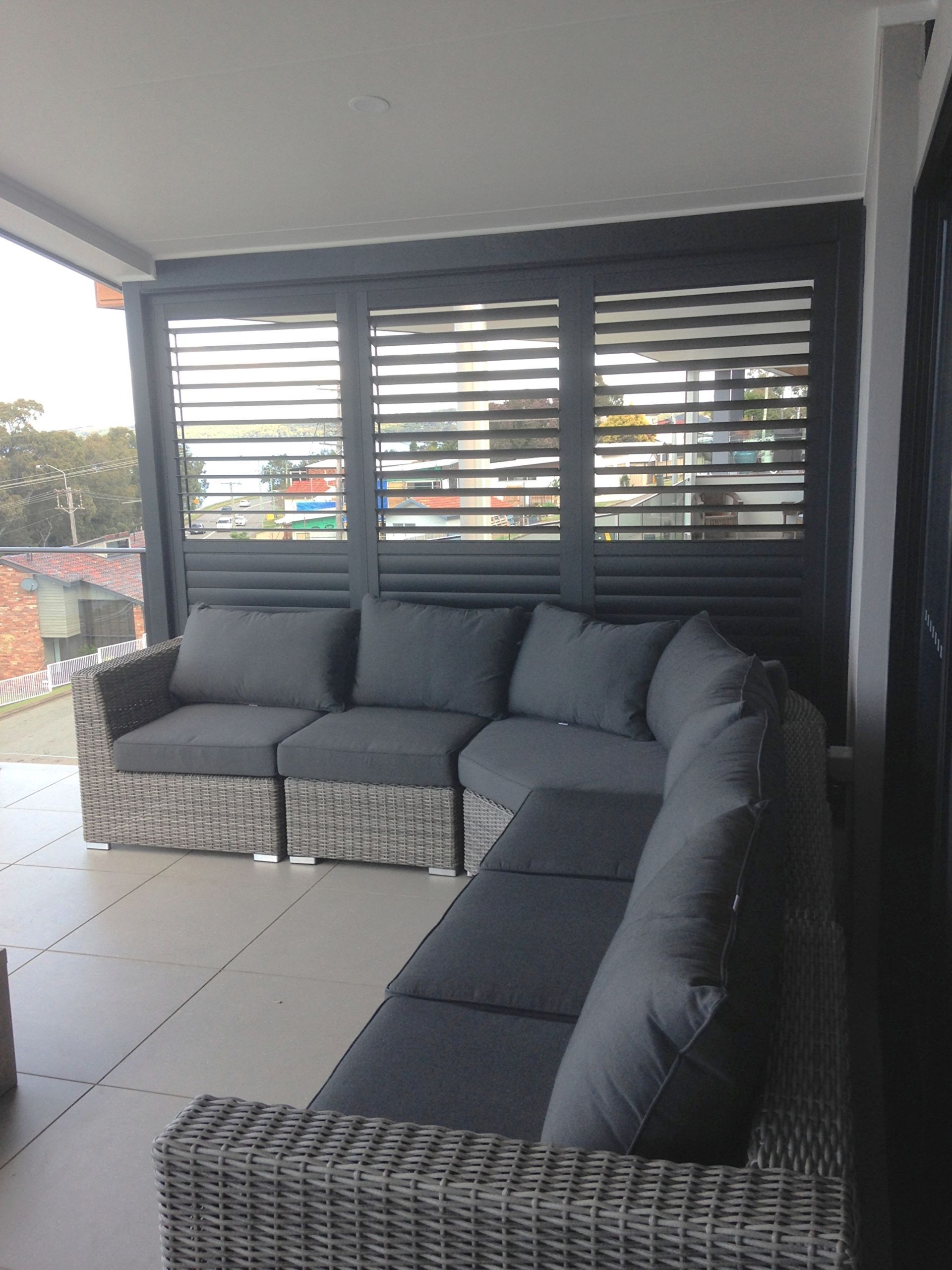 Covered patio with dark gray wicker sectional sofa and ottoman by louvered windows.
