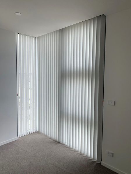 White Vertical Blinds Cover A Corner Window In A Room — Winning Blinds in Cardiff, NSW