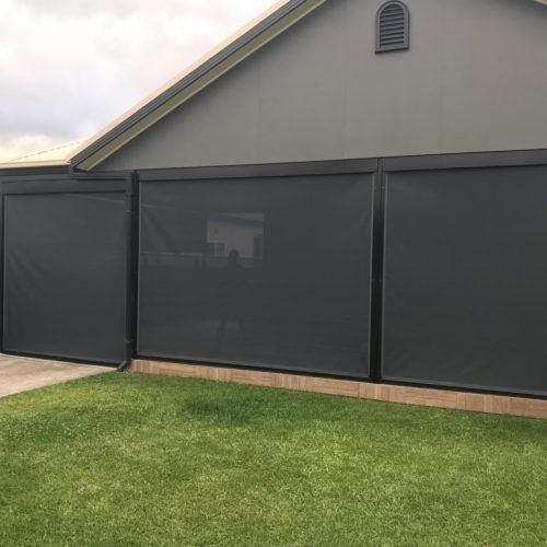 Black Awnings in the front of a dark grey house with grass in the front — Winning Blinds in Cardiff, NSW