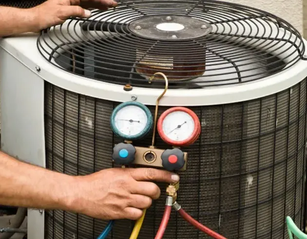 Technician checking HVAC unit pressure gauges with hoses attached to the outdoor condenser.