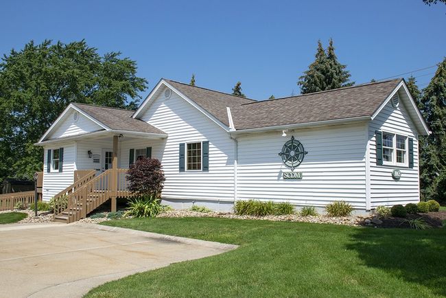 White house with green lawn, blue shutters, and wooden porch under a sunny sky.