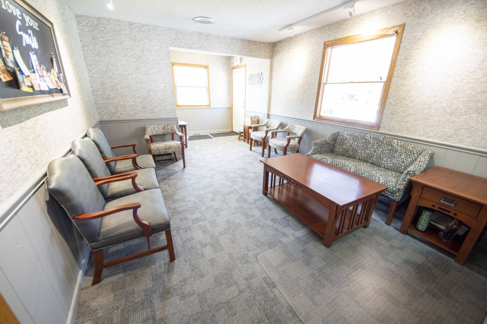 Waiting room with gray carpet, chairs, sofa, coffee table, and windows.