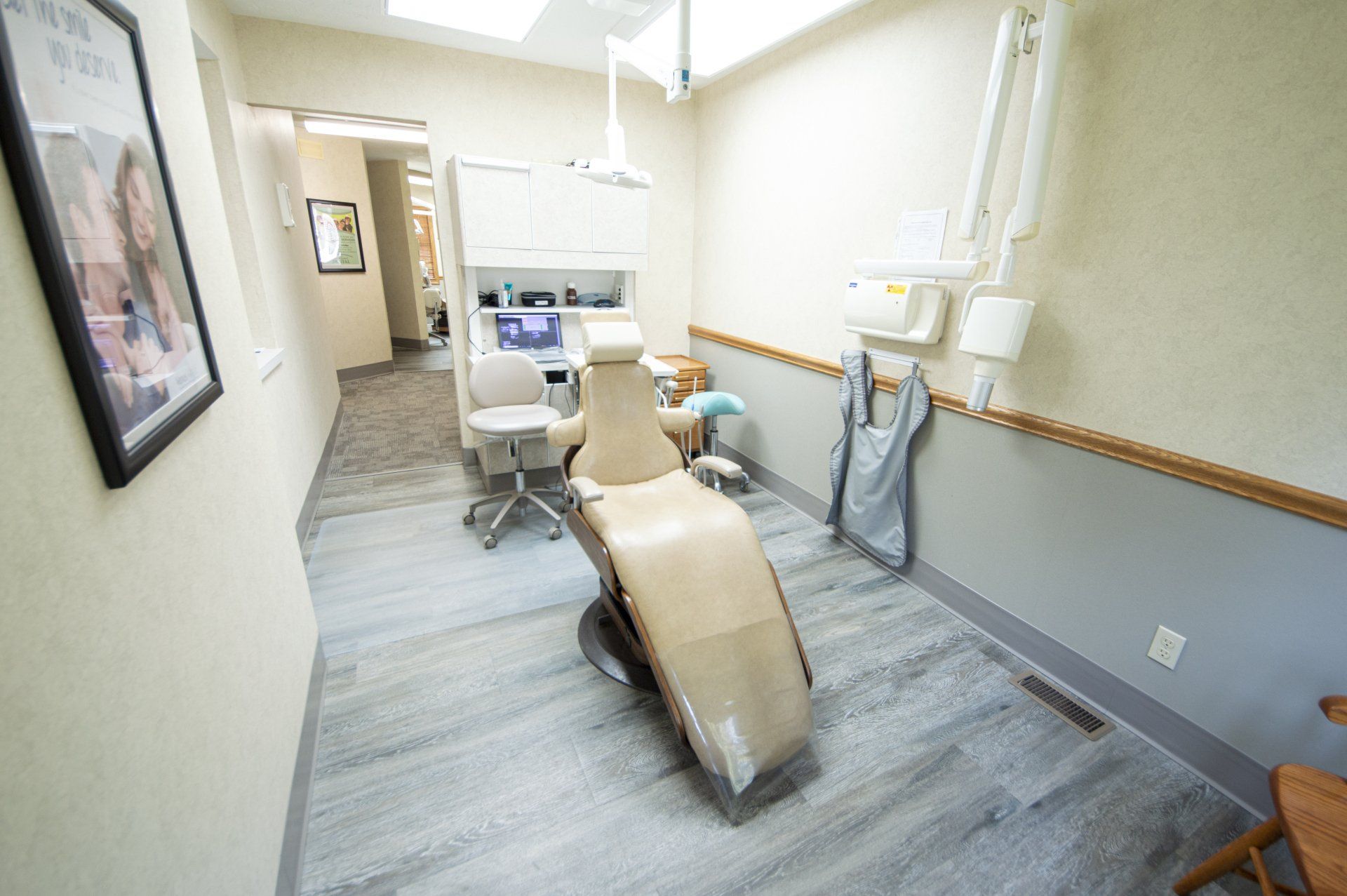 Dental operatory with chair, light, and equipment; light beige walls and gray flooring.