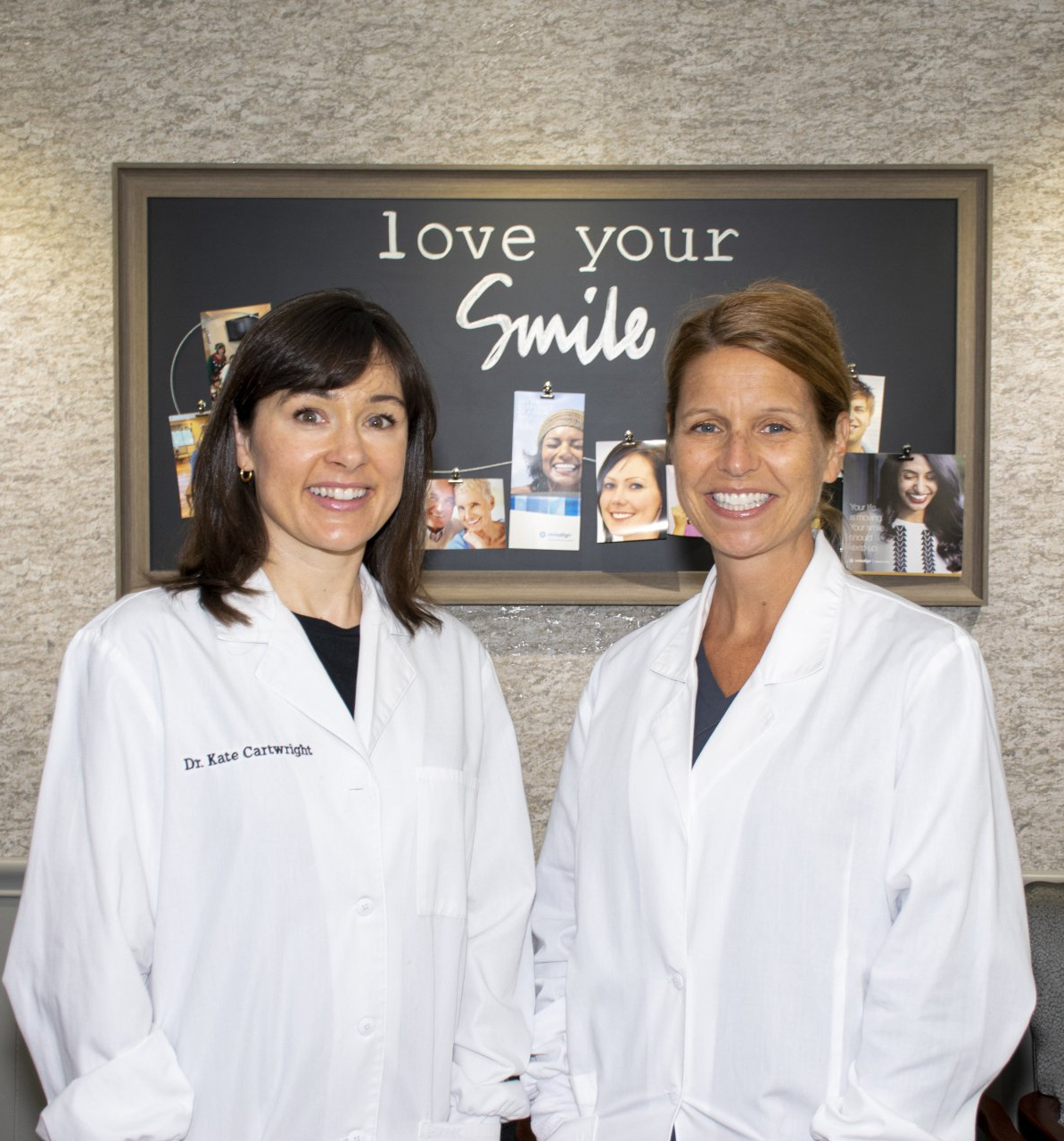 Two women in lab coats stand in front of a sign that says 