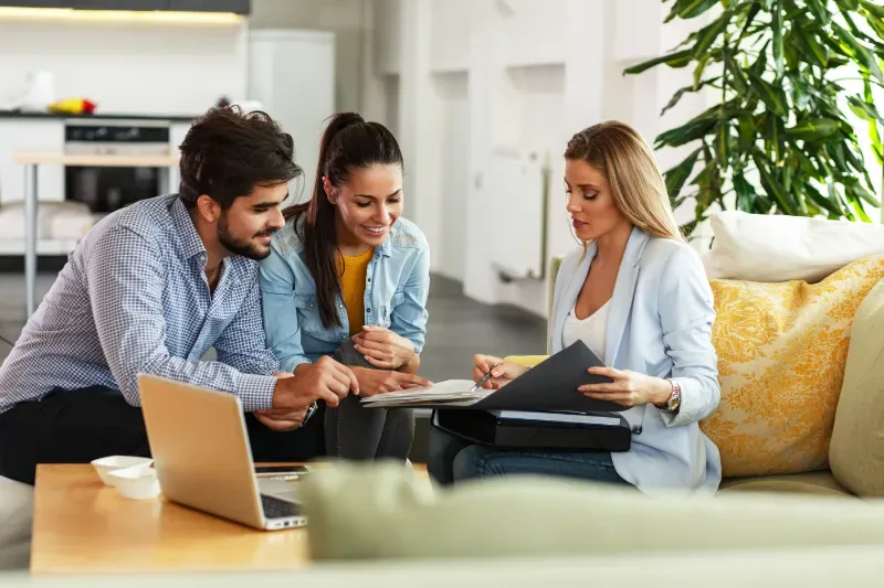 A man and a woman are sitting on a couch talking to a real estate agent.
