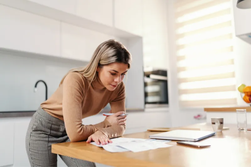 A woman is sitting at a table in a kitchen looking at papers.