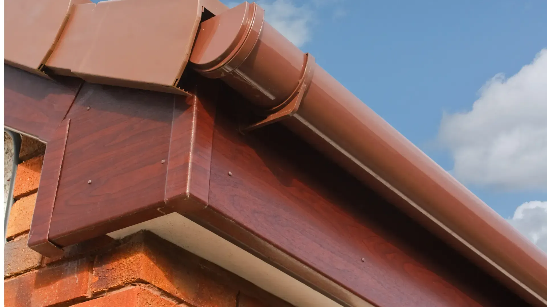Close-up of a brown roof gutter and tiles against a blue sky with clouds