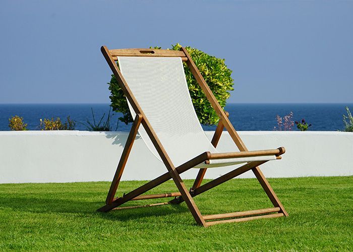 A lawn chair is sitting in the grass with the ocean in the background