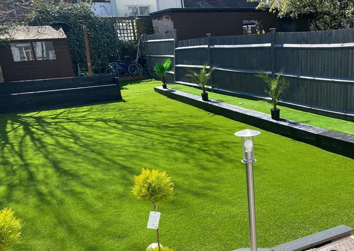 A lush green lawn with a fence and a shed in the background.