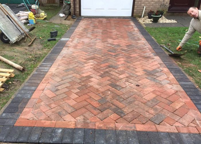 Herringbone brick block paving driveway in Woking, featuring a dark border, with a worker and tools nearby, by Surrey Hills.