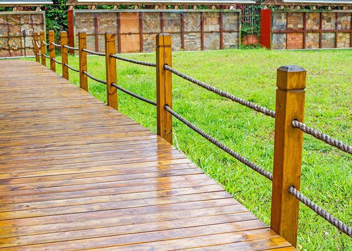 A wooden walkway with a rope fence leading to a grassy field.