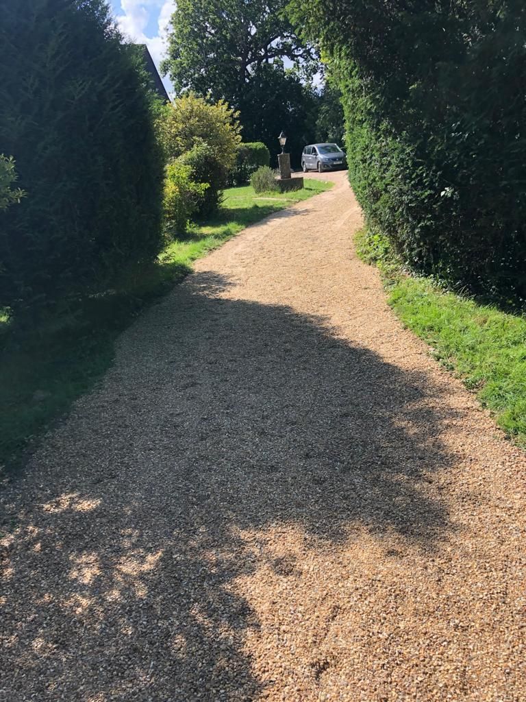 A gravel driveway with a car parked on the side of it.