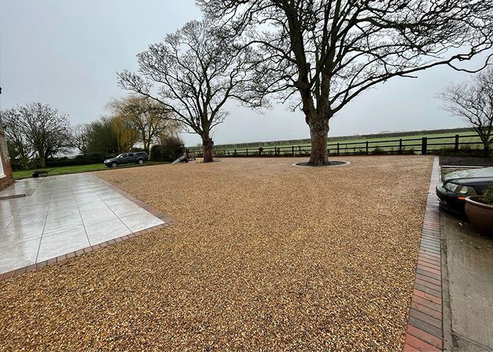 A gravel driveway with cars parked in it and trees in the background.