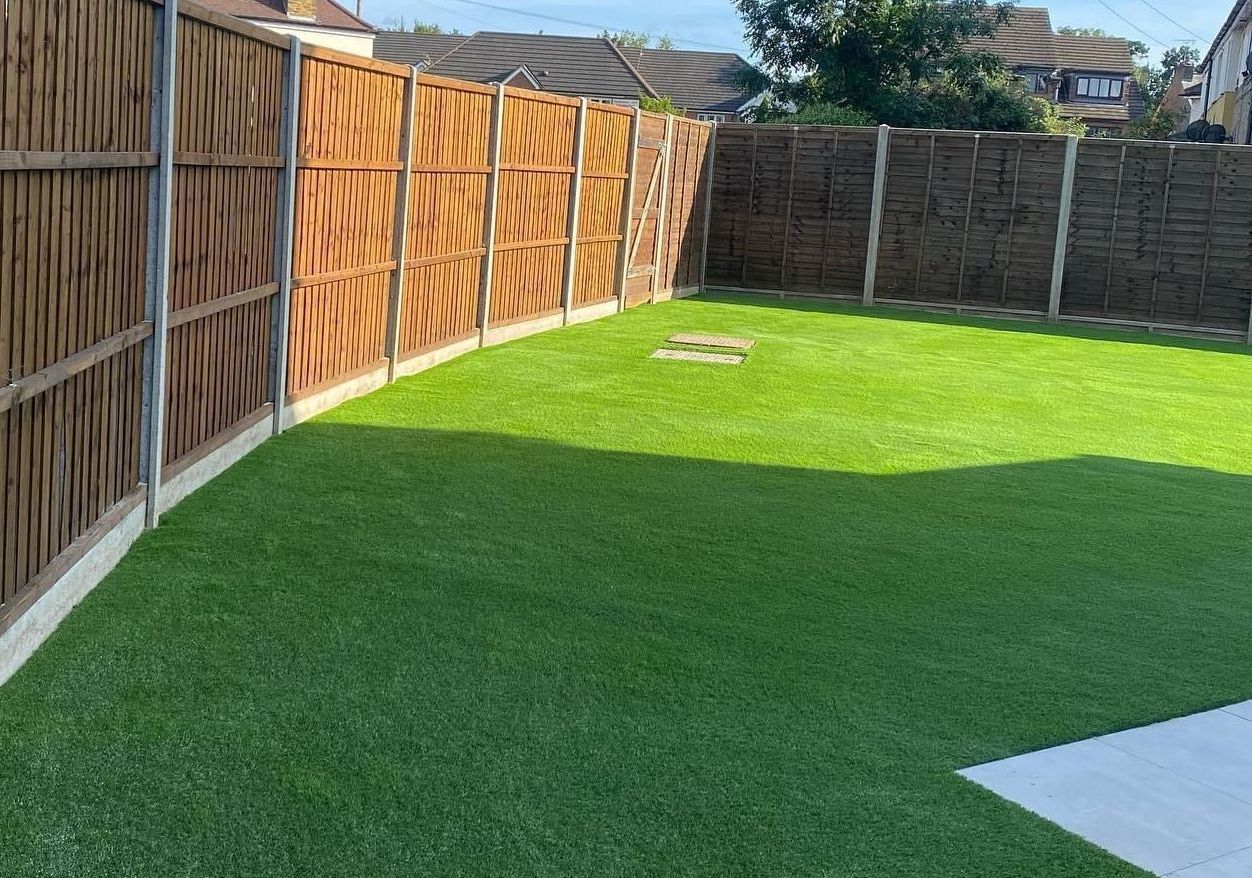 A backyard with a wooden fence and a lush green lawn.