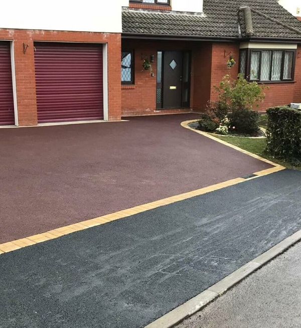 A driveway in front of a brick house with a red garage door