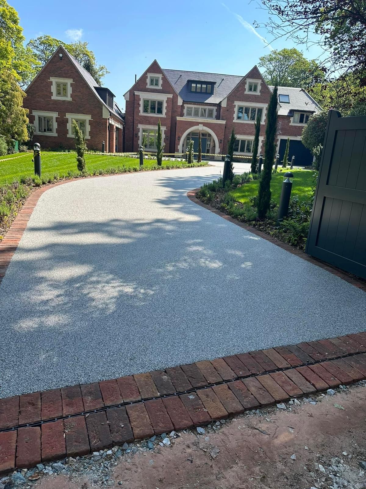 Luxury resin-bound driveway in Woking by Surrey Hills, curving towards a grand house, bordered by brick and landscaping.