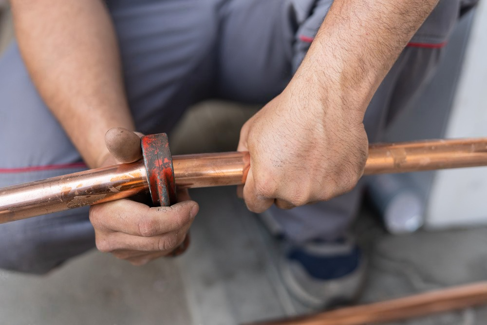 a man is cutting a copper pipe with a pair of scissors .