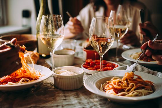 A group of people are sitting at a table eating spaghetti and drinking wine.
