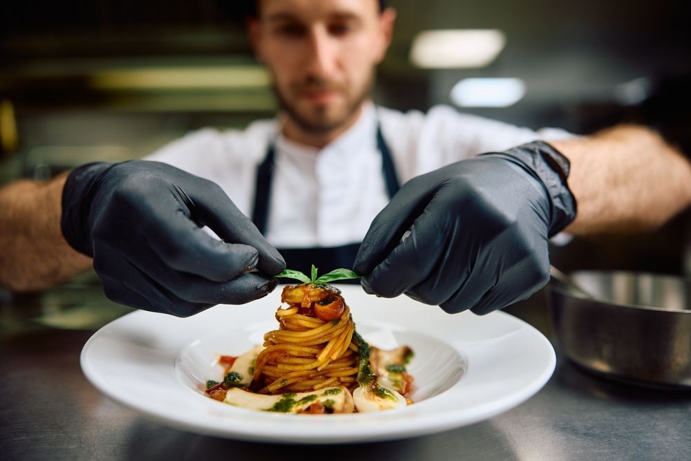 A chef wearing black gloves is preparing a plate of food.