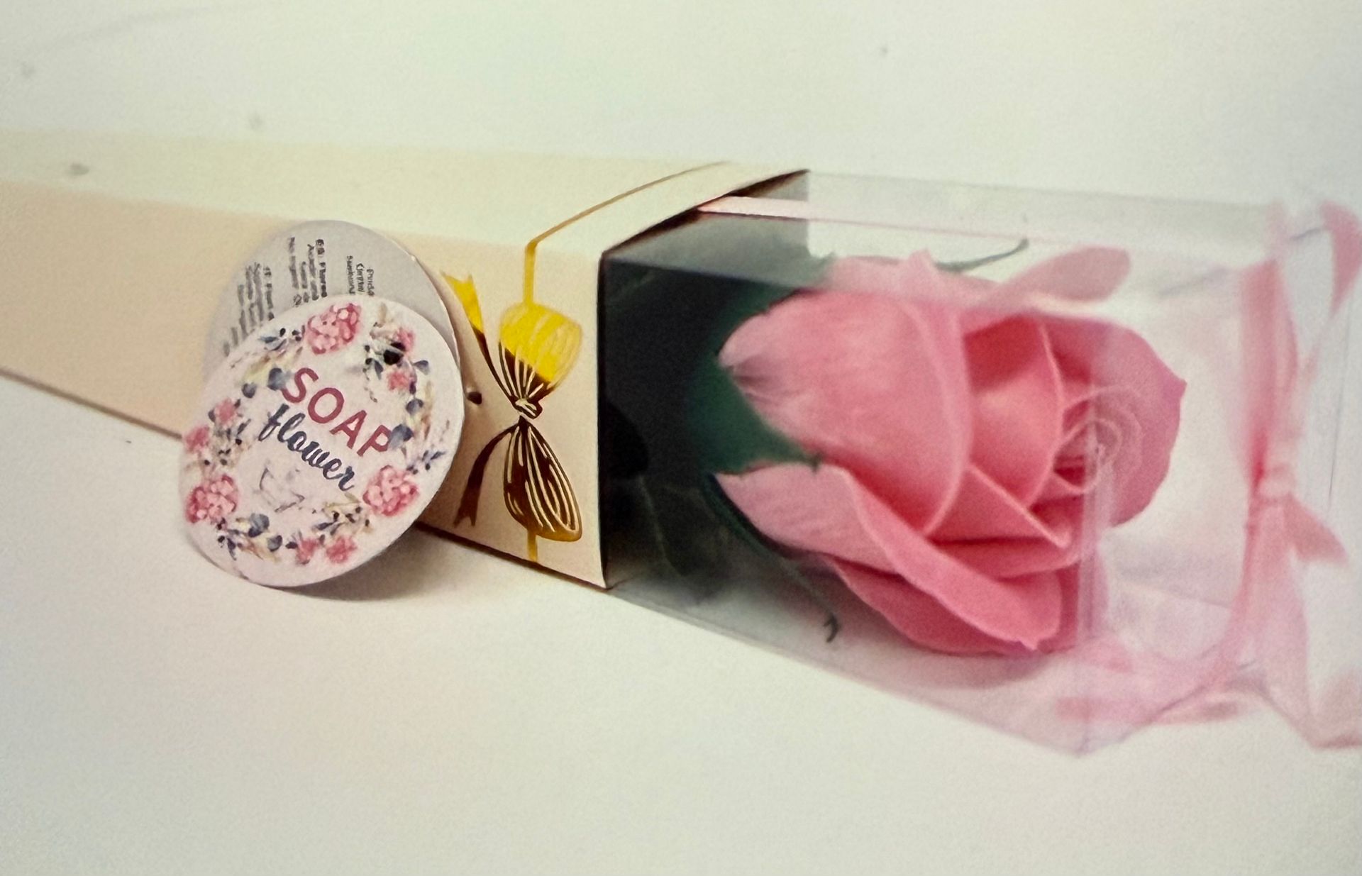 Vier zeepbloemen in de vorm van rozen, verpakt in een transparante verpakking met lint en decoratieve labels.
