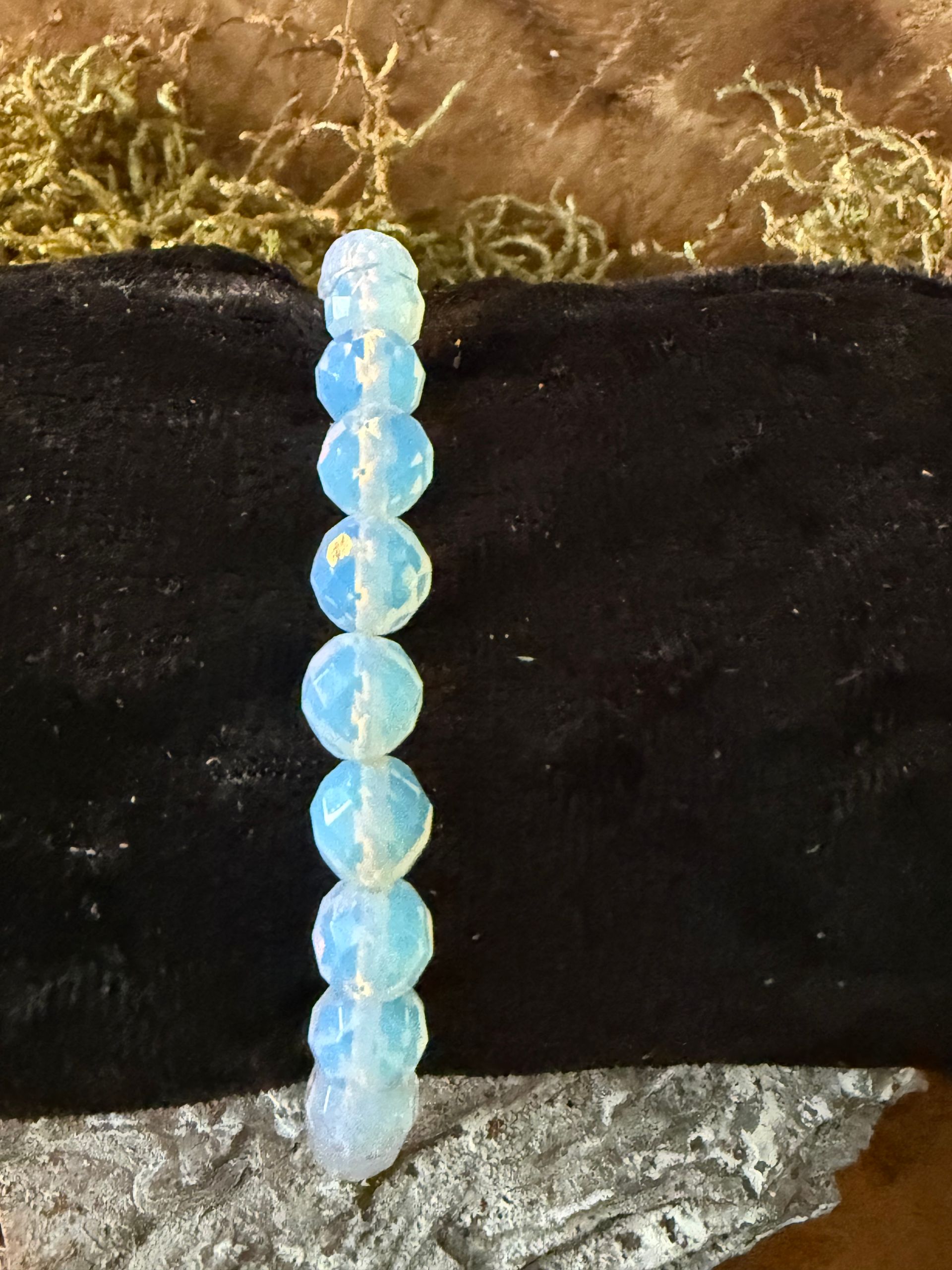 Lichtblauwe kralenarmband op een zwart, gestructureerd blok; tentoongesteld op hout, boomschors en dennenappels.
