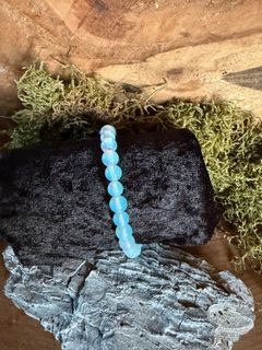 Blauwe kralenarmband op een zwarte, gestructureerde ondergrond, met een achtergrond van rotsen en mos.