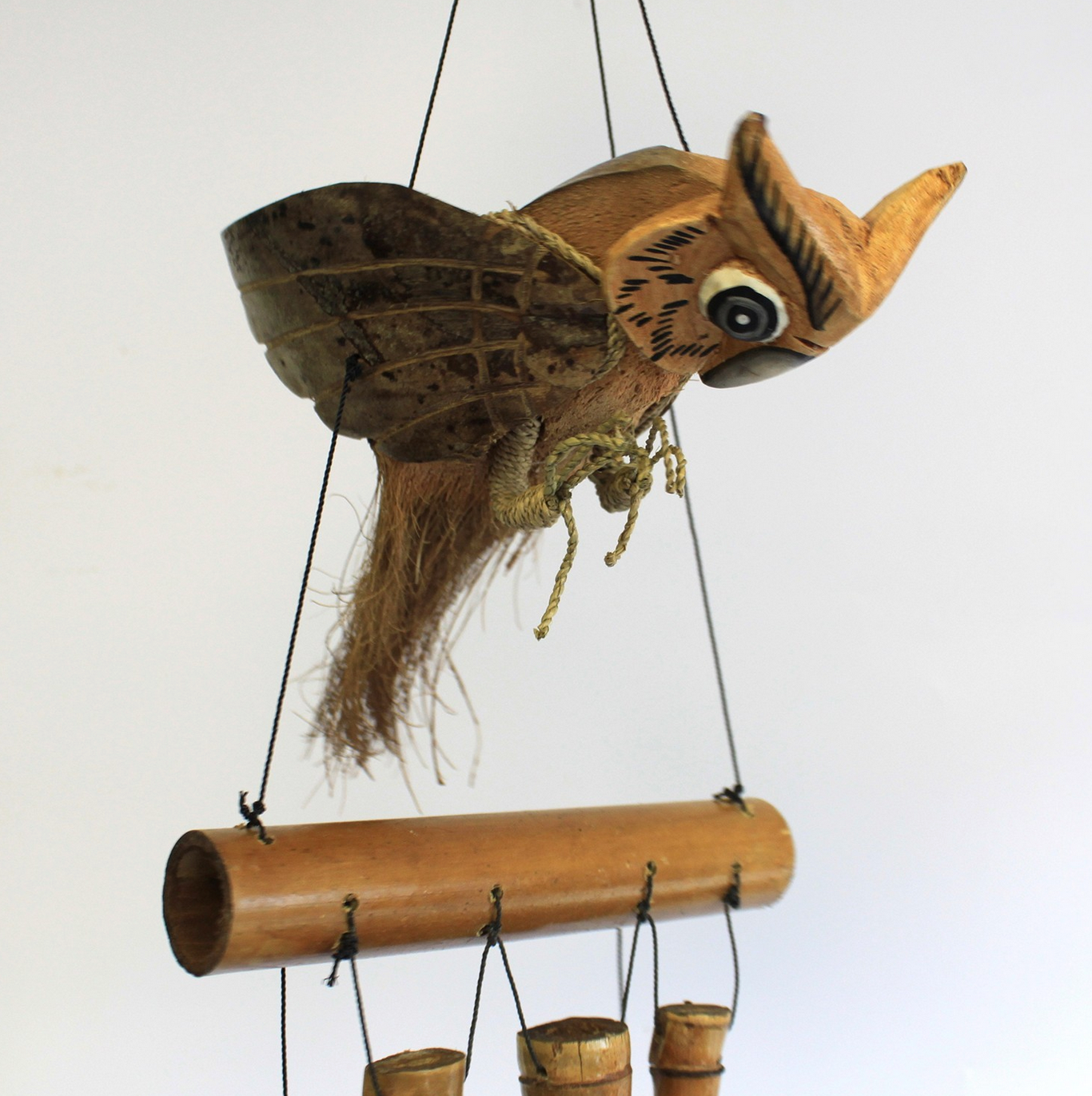 Een windgong in de vorm van een uil in een tuin. Bruine en beige kleuren. Bamboe buizen hangen eronder.