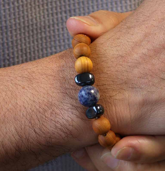 Close-up van een pols met een kralenarmband; afwisselend hout en blauwe en zwarte stenen.