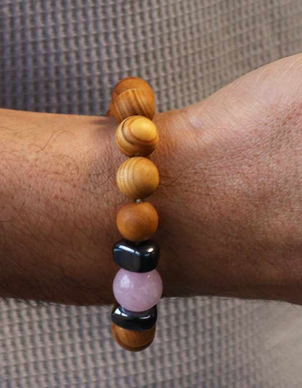 Close-up van de pols van een persoon die een kralenarmband draagt met houten en edelstenen kralen.