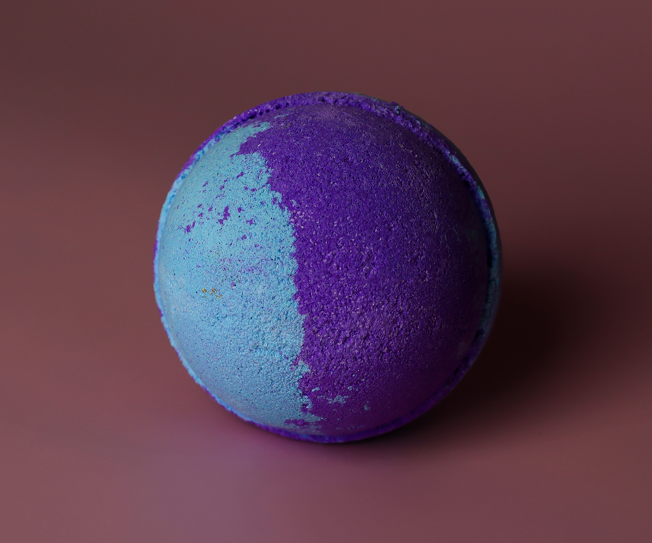 Een ronde bruisbal, half blauw en half paars, ligt op een bruine ondergrond.
