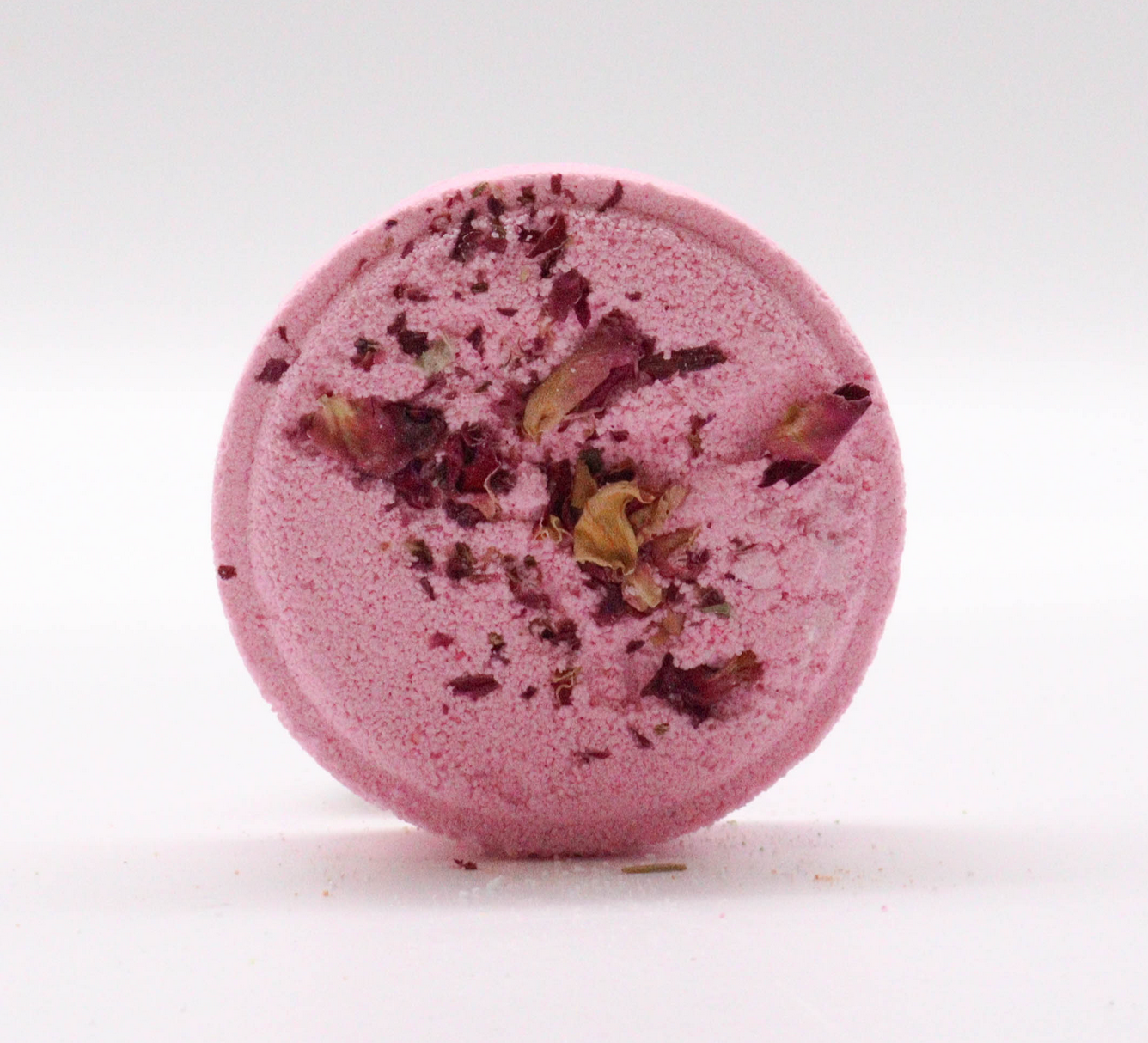 Roze bruisbal voor in bad met rozenblaadjes, omringd door bloemen, bladeren en bessen.